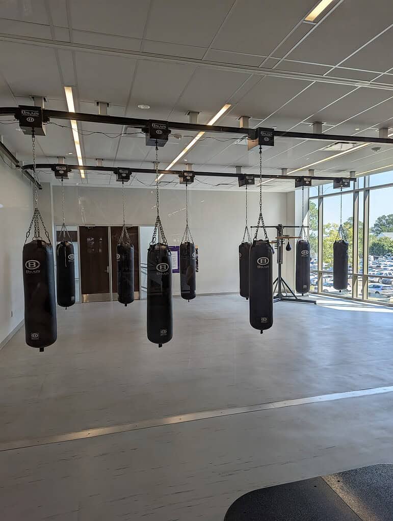 Eleven Balazs heavy bags deployed on an Ultra-Trak ceiling track in a university training studio with a glass curtain wall