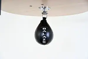 Black Balazs Lazer 8 x 5 inch peanut speed bag, Balazs-logo view, mounted beneath a wooden platform