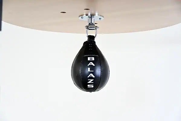 Black Balazs Lazer 8 x 5 inch peanut speed bag, Balazs-logo view, mounted beneath a wooden platform